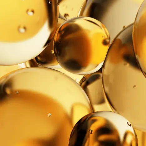 Eine Ansammlung glänzender, goldfarbener Kugeln ist dicht beieinander. Die Oberfläche reflektiert Licht und erzeugt einen schimmernden Effekt. Einige Kugeln haben kleine Wassertropfen, die darauf sitzen, was einen zusätzlichen glänzenden Kontrast bietet.